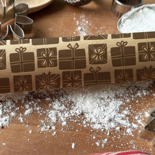 Wooden rolling pin with embossed patterns on a wooden surface with flour, branded 'Pickle and Peach Studio'.