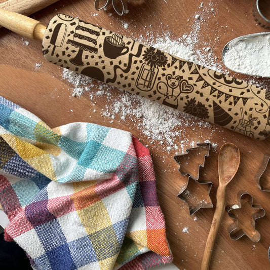 Decorative rolling pin with embossed designs on a wooden surface with flour and baking tools.