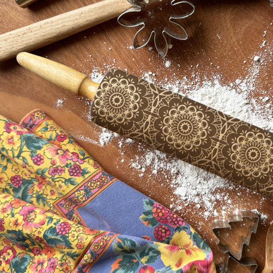 Decorative rolling pin with floral patterns on a wooden surface with flour and baking tools.