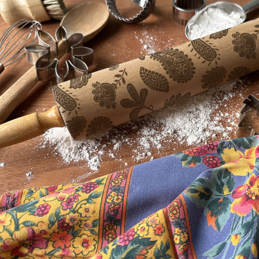 Floral-patterned rolling pin on a wooden surface with baking tools and flour.