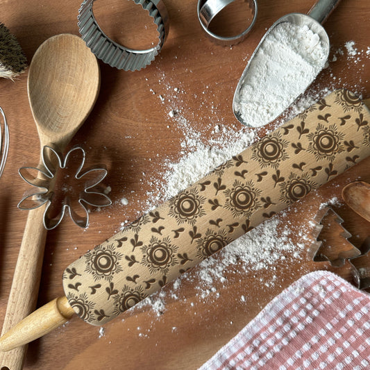 Decorative rolling pin with floral patterns on a wooden surface with flour and baking tools.