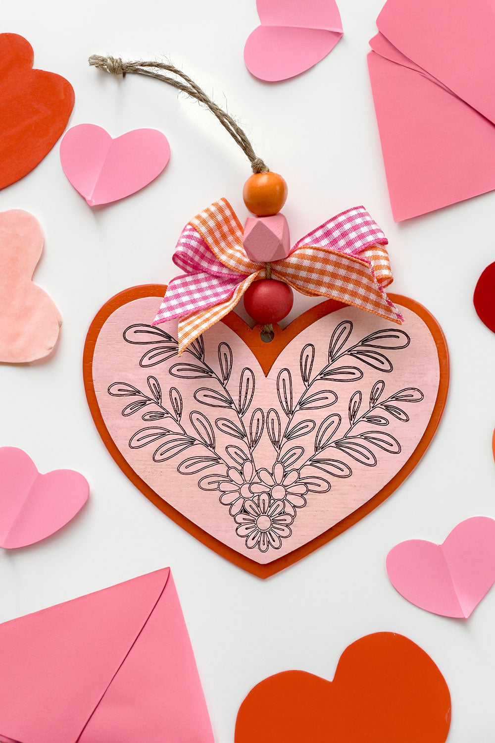 A laser cut heart ornament in pink and red with a leafy floral design.
