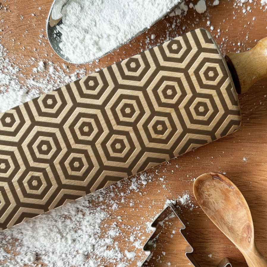 Wooden rolling pin with geometric pattern and cookie cutters on a wooden surface with flour, branded 'Pickle and Peach Studio'.