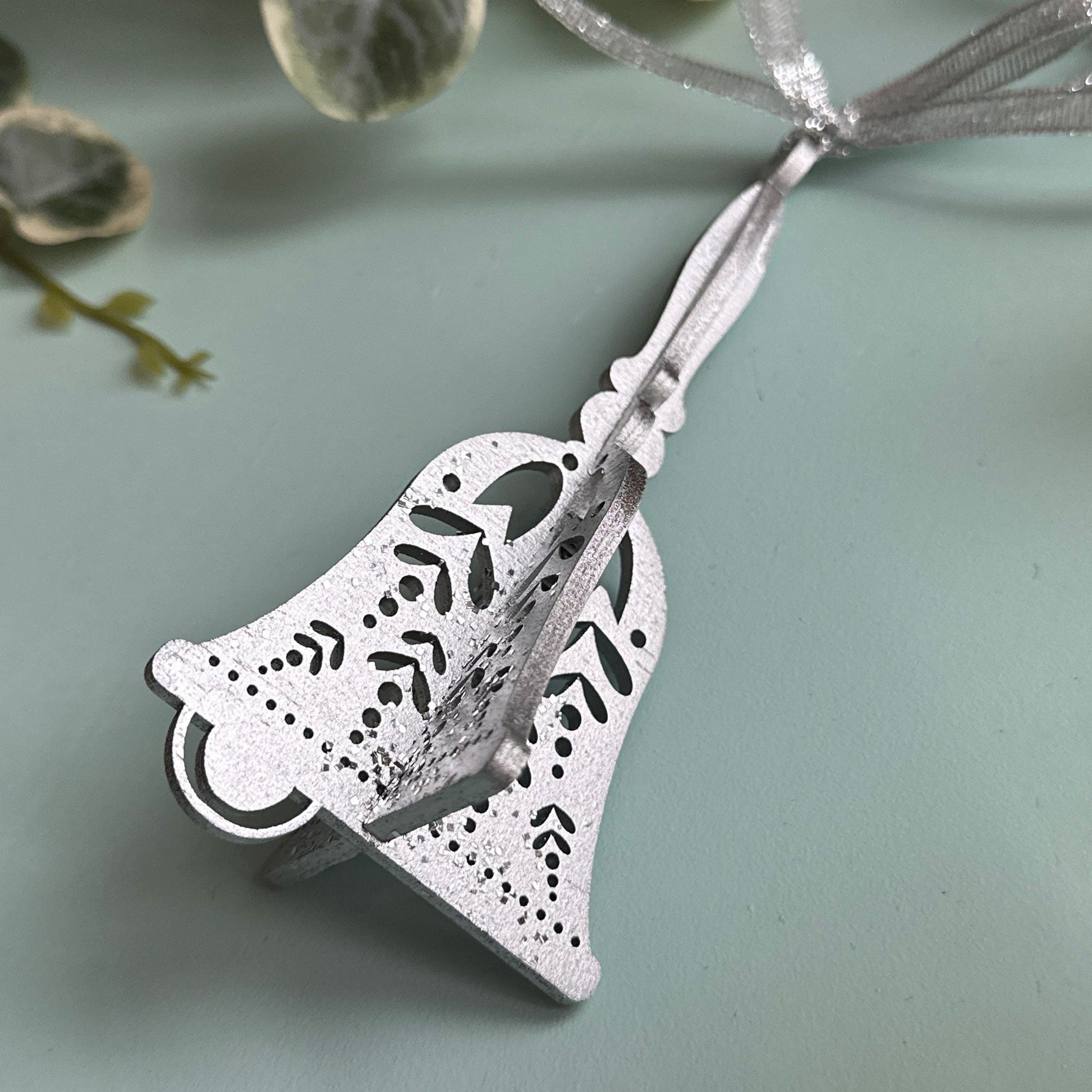 Silver bell-shaped pendant on a light blue background with green leaves.