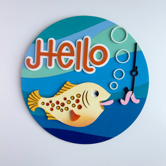 Circular decorative item with a fish and 'Hello' text on a blue background