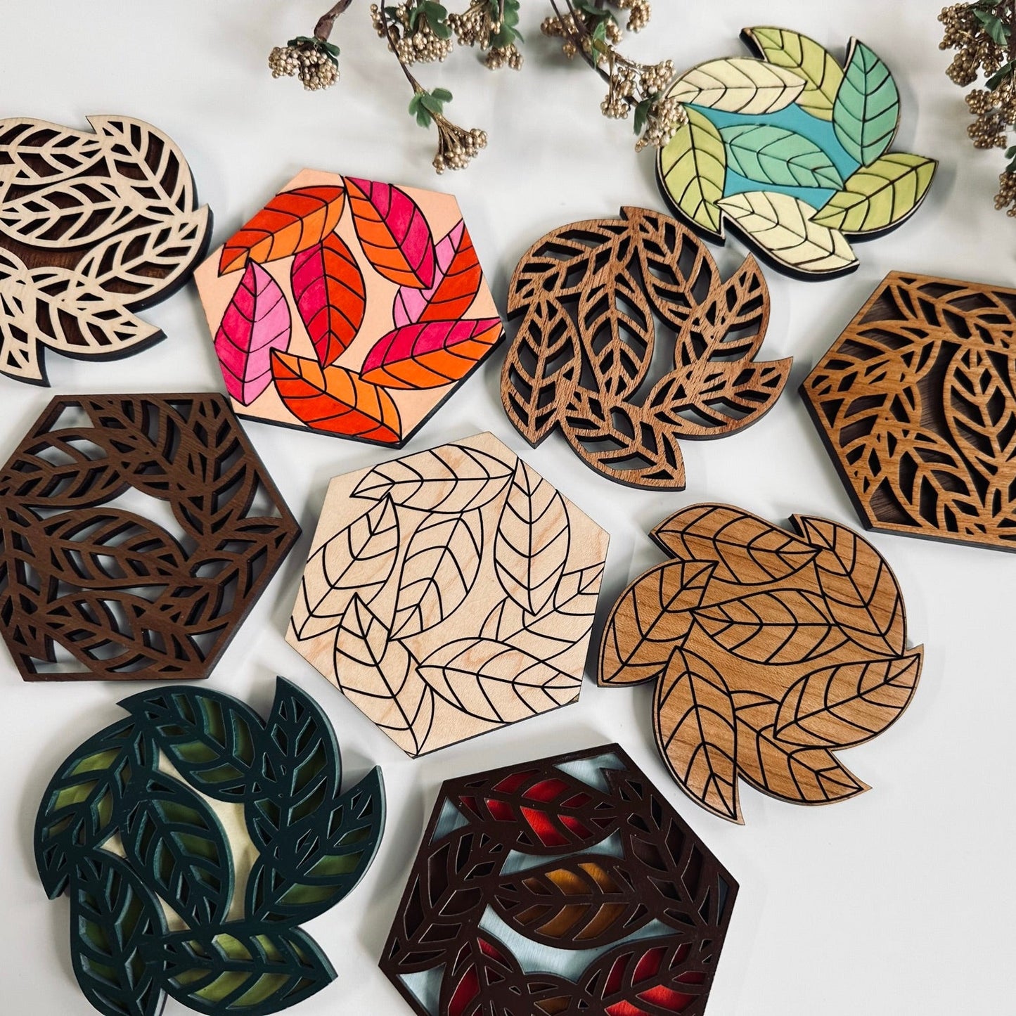 Collection of leaf-shaped wooden coasters in various colors on a white background.