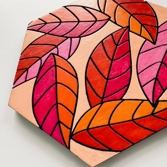 Hexagonal wooden coaster with colorful leaf pattern on a light gray background