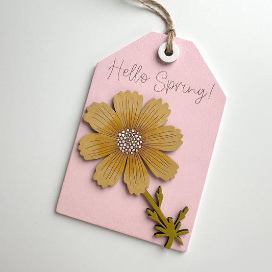 Pink tag with a yellow flower design and 'Hello Spring!' text on a light gray background