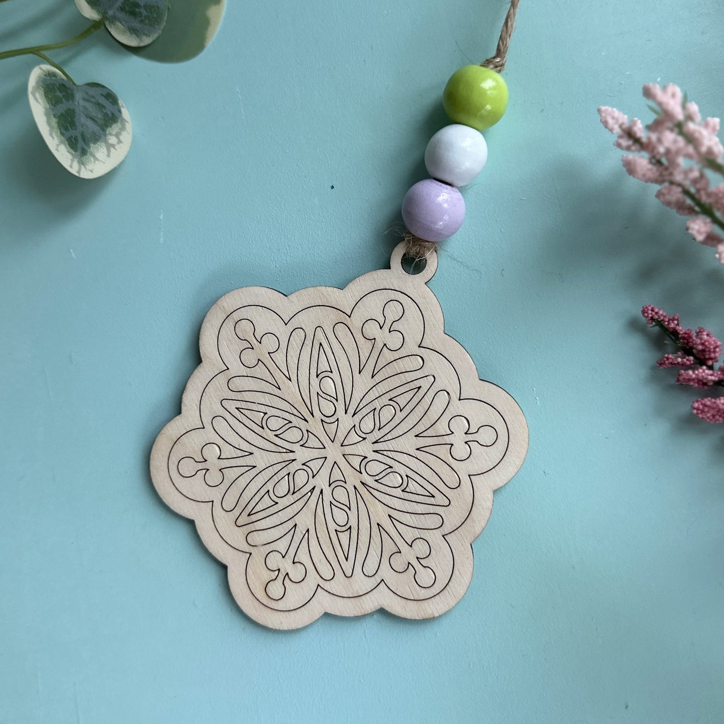Decorative wooden tag with intricate patterns on a light blue background with plants.