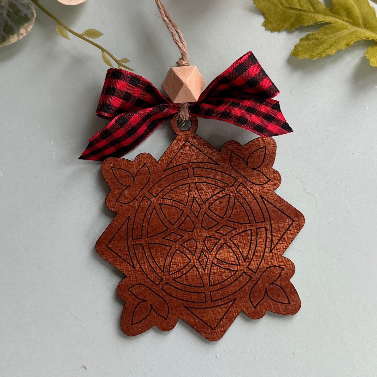 Decorative wooden ornament with a red and black checkered bow on a light background with flowers and leaves.