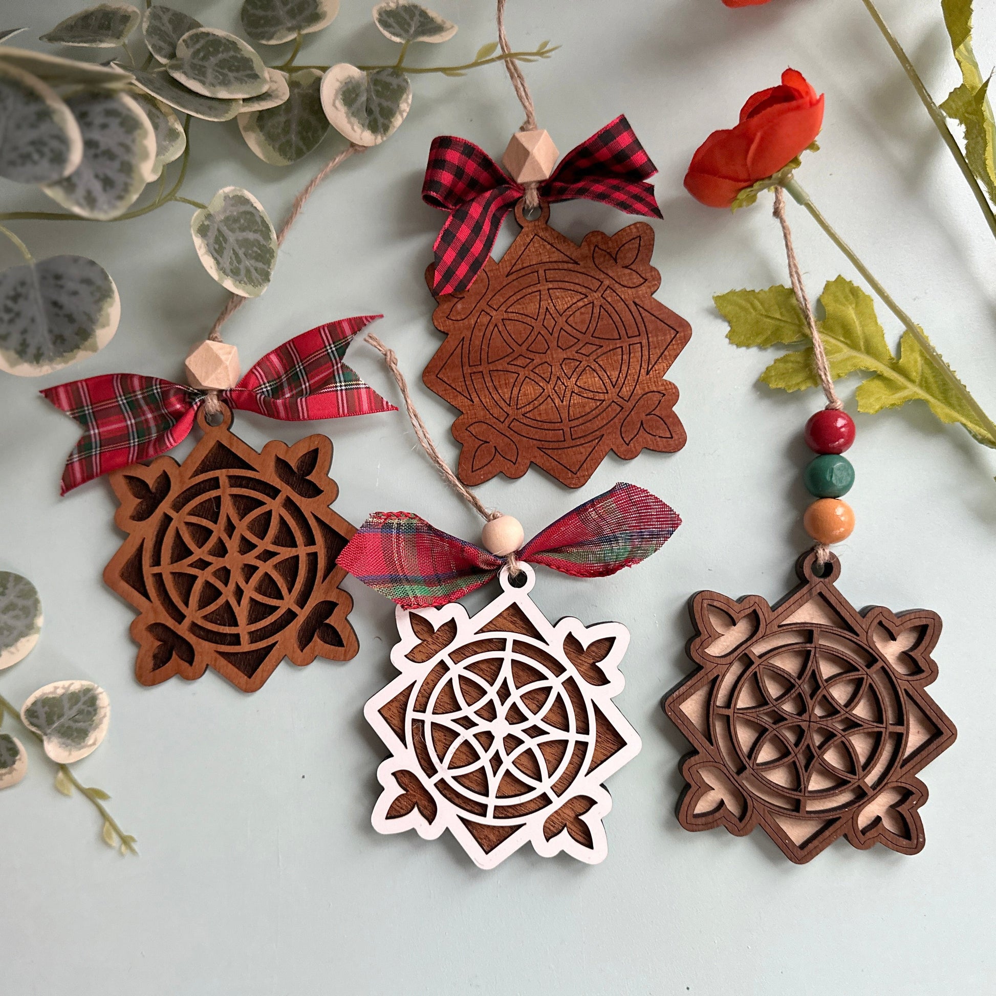 Decorative wooden ornaments with intricate designs on a white surface with greenery.