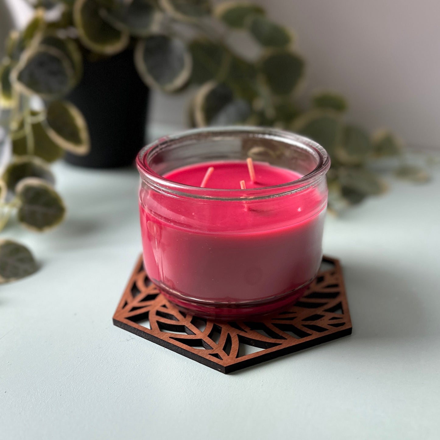Red candle on a decorative trivet with leaves and a photo frame in the background