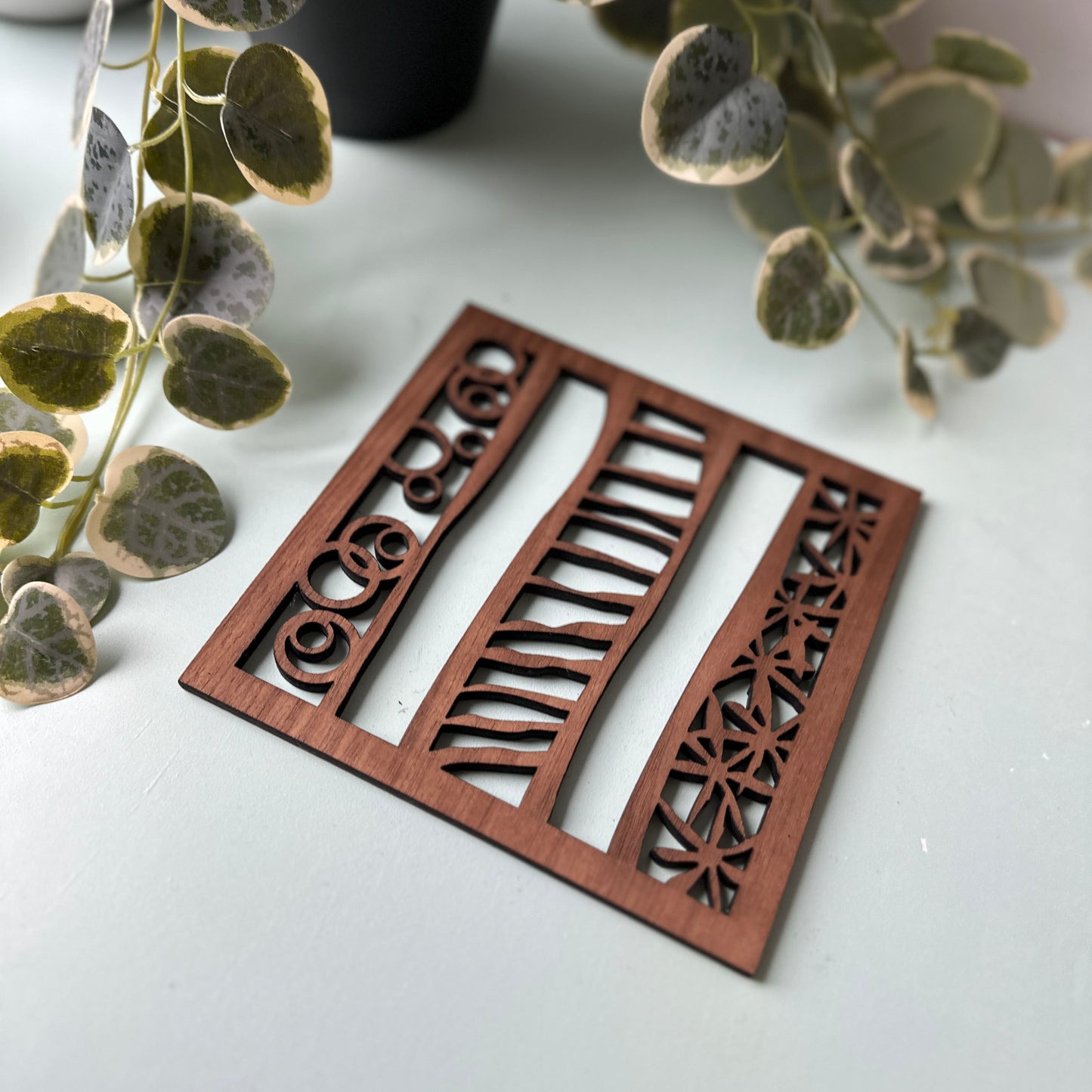 Decorative wooden trivet with intricate carvings on a light surface with plants in the background