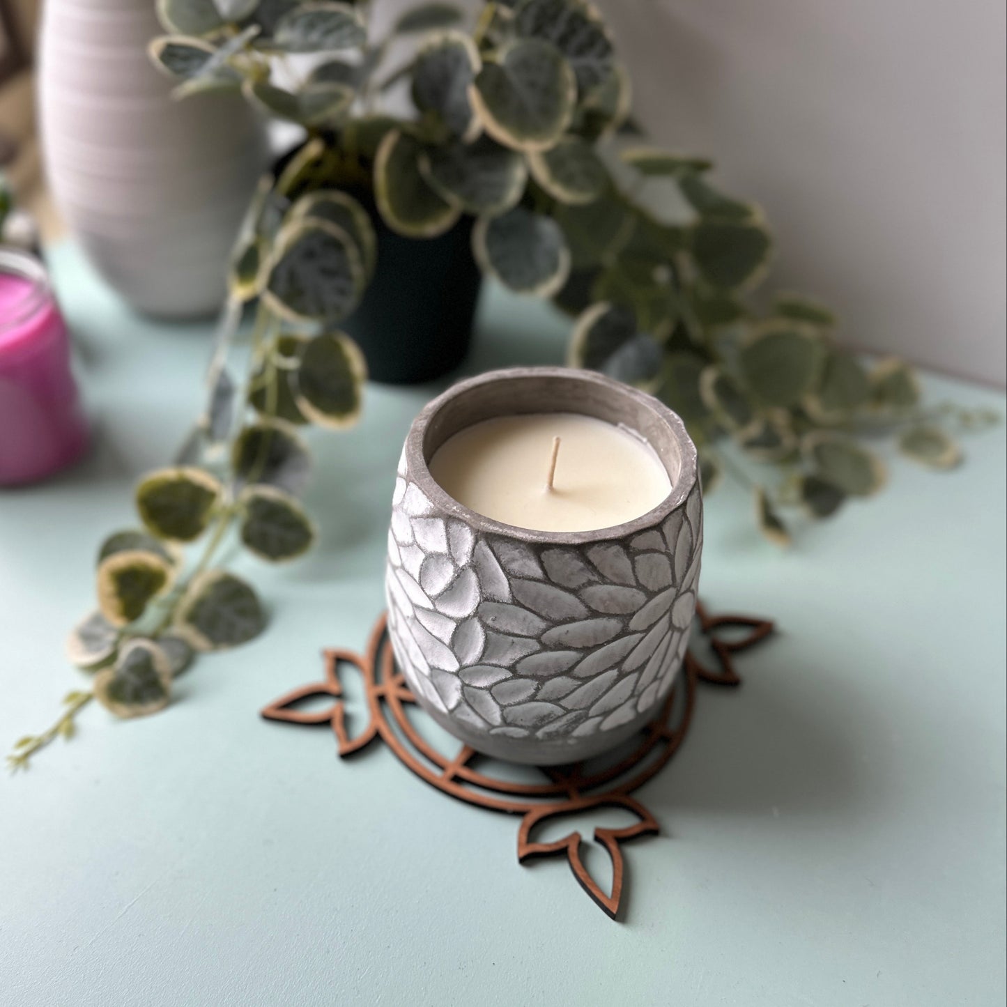 White candle in a decorative glass holder on a stained glass trivet with leaves in the background