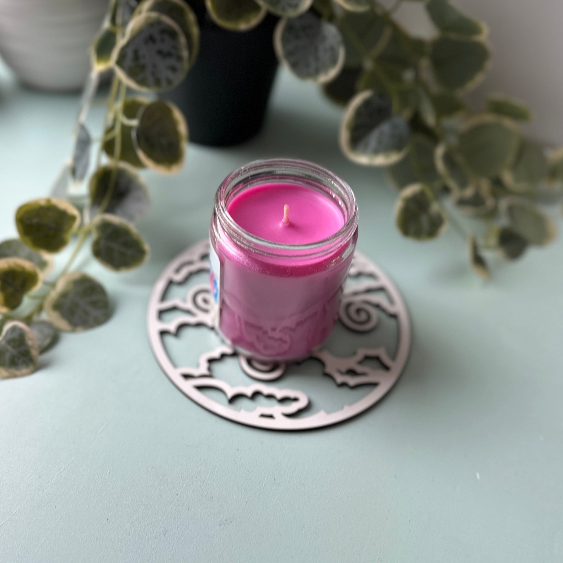 Pink candle on a decorative trivet with green leaves in the background
