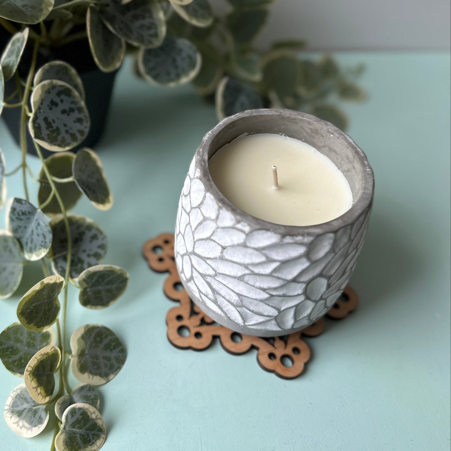Ceramic candle holder with a lit candle on a light surface next to a plant