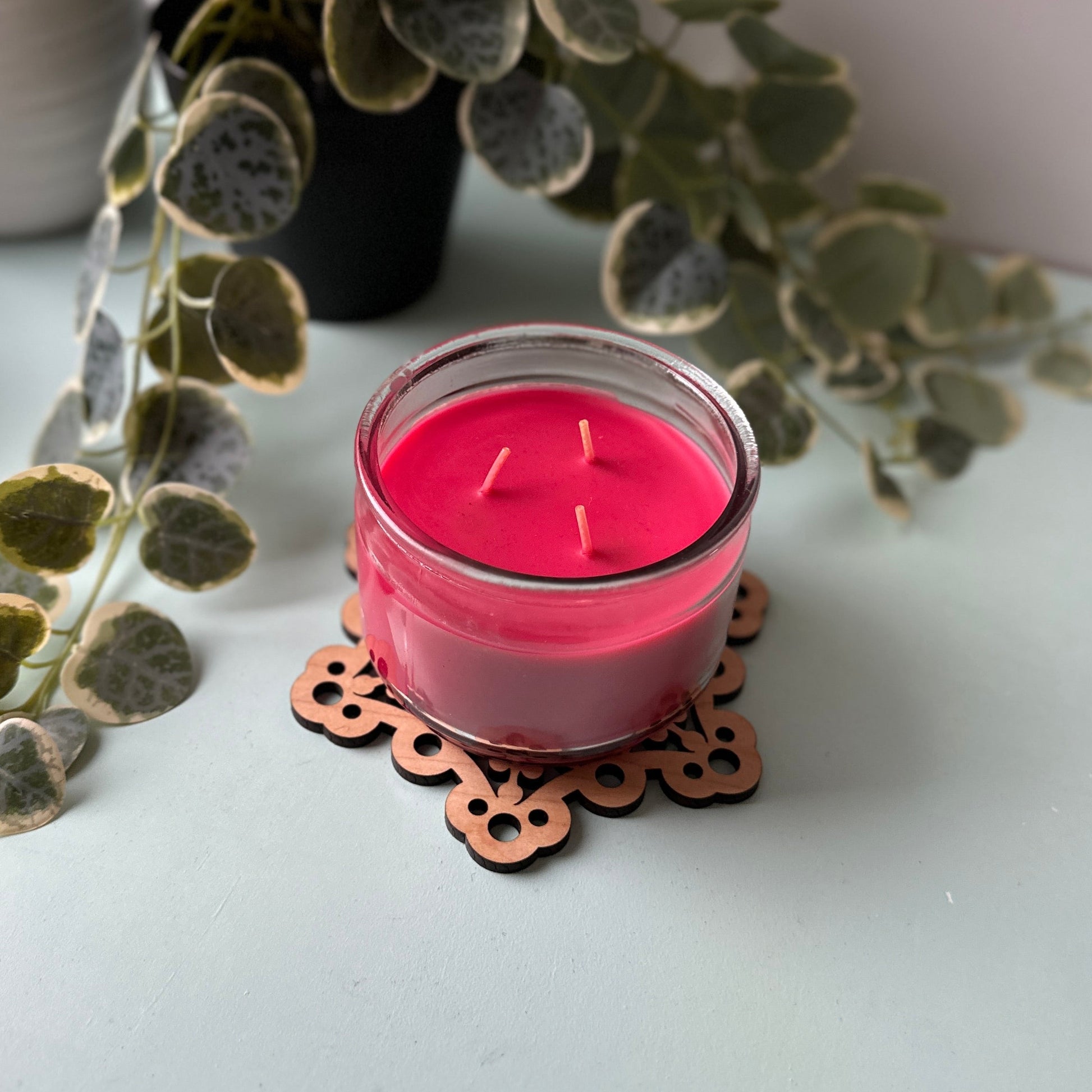 Pink candle on a decorative trivet with plants in the background