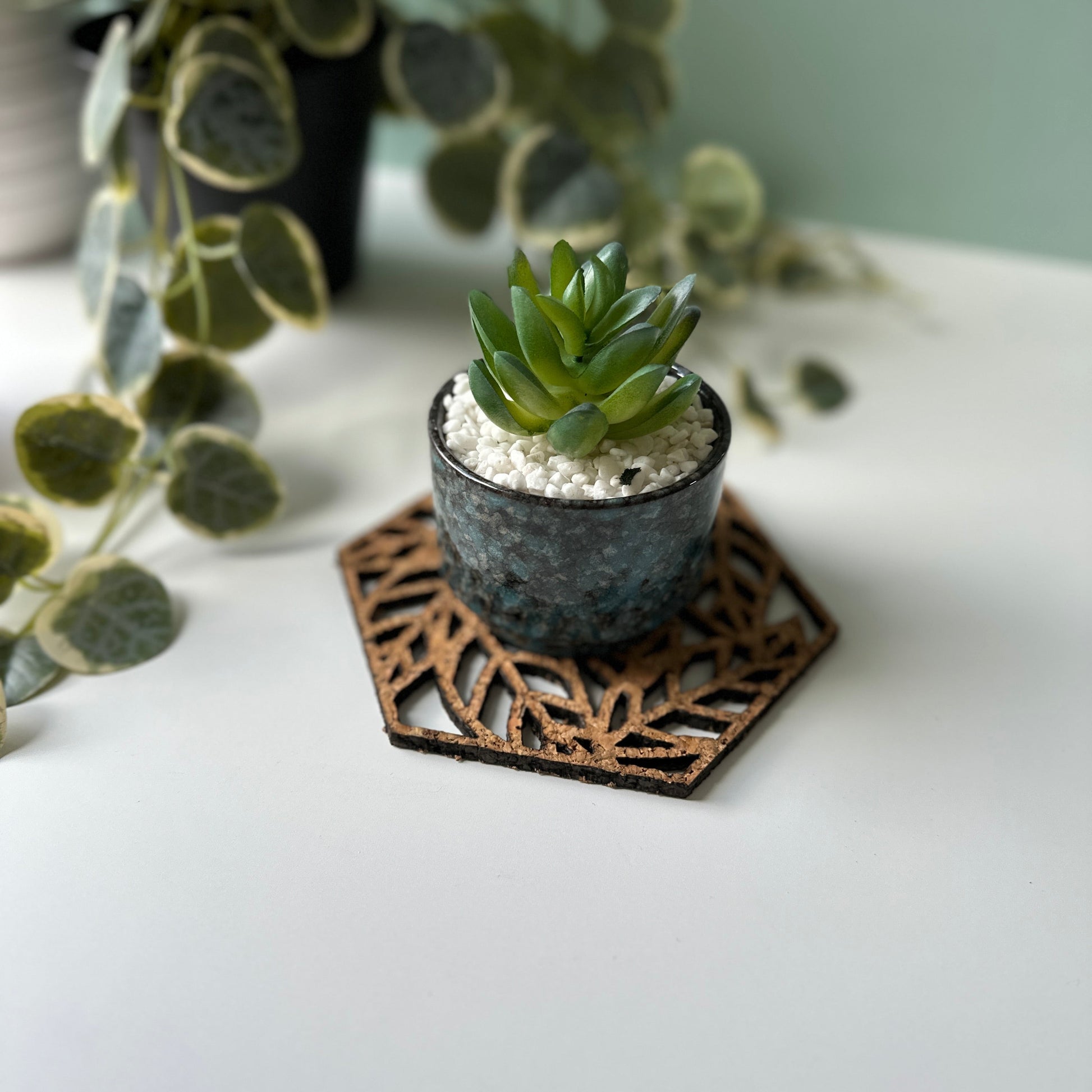 A plant on a decorative trivet with a leaf design and a photo frame in the background