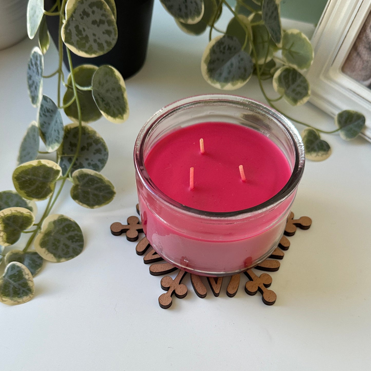 Pink candle on a trivet on a white surface with greenery
