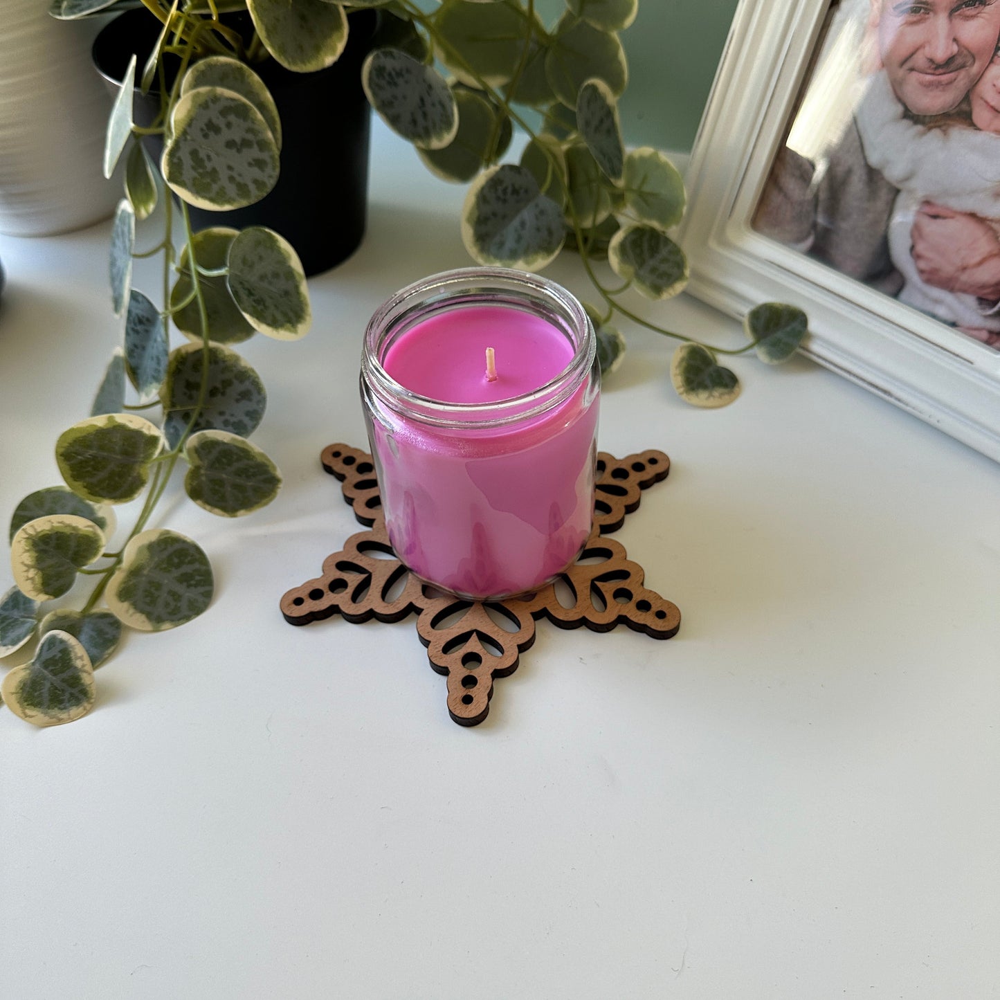 Pink candle on a decorative trivet with a plant and mirror in the background