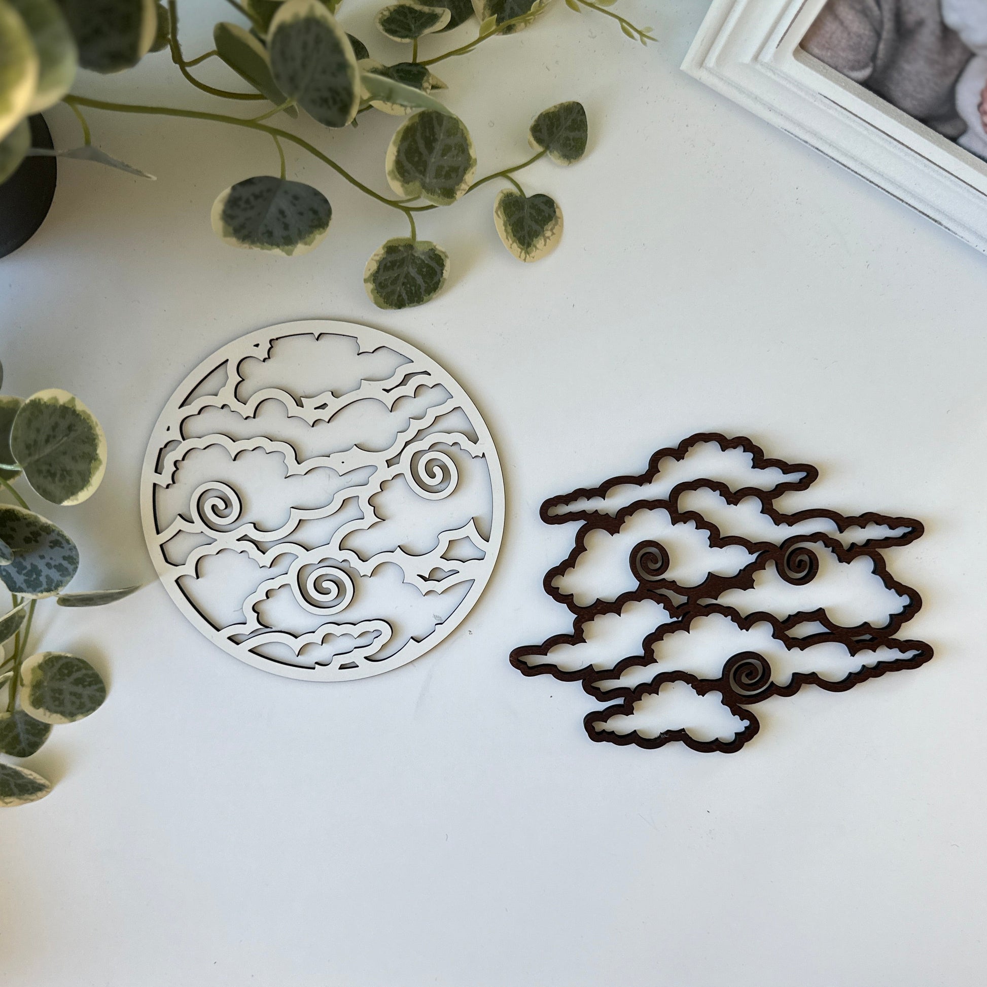 Decorative cloud trivets on a white surface with a plant and photo frame in the background.