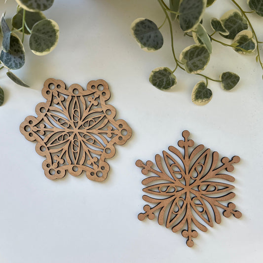 Two wooden snowflake trivets on a white surface with green leaves.