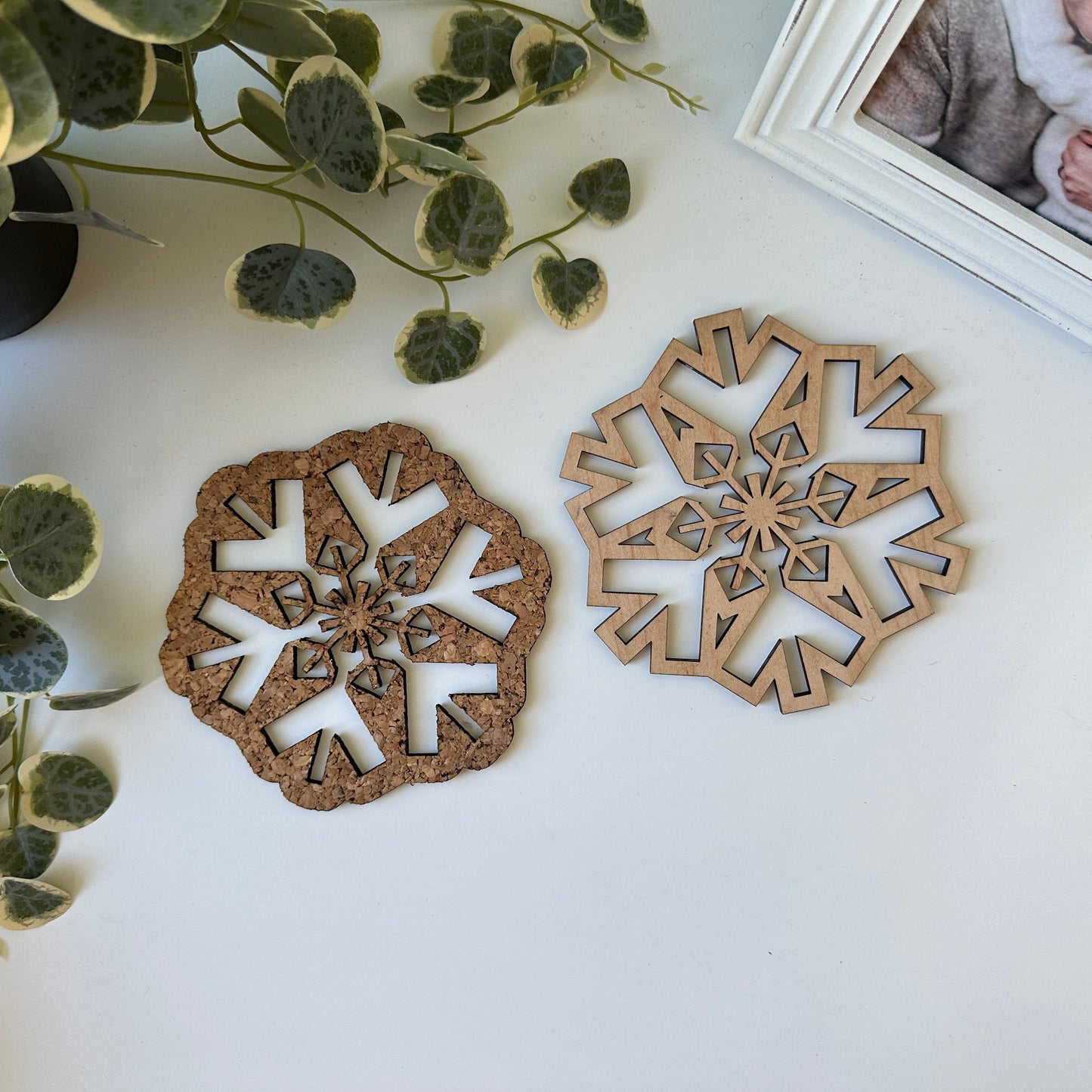 Two snowflake trivets on a white surface with greenery and a photo frame in the background.