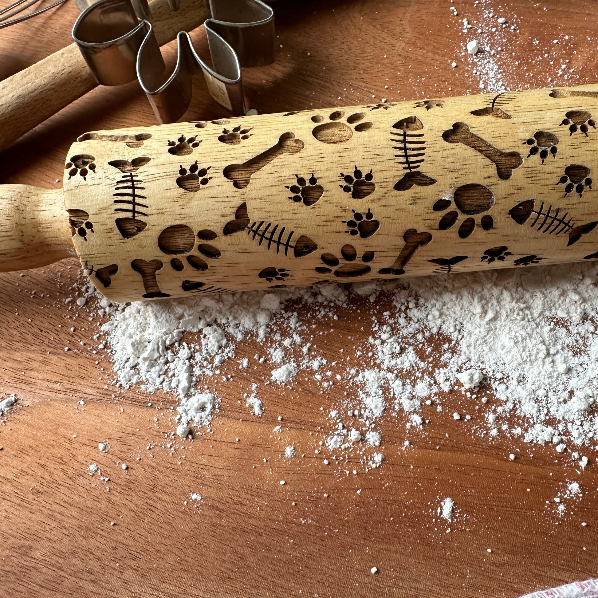 Wooden rolling pin with embossed designs on a wooden surface with flour.