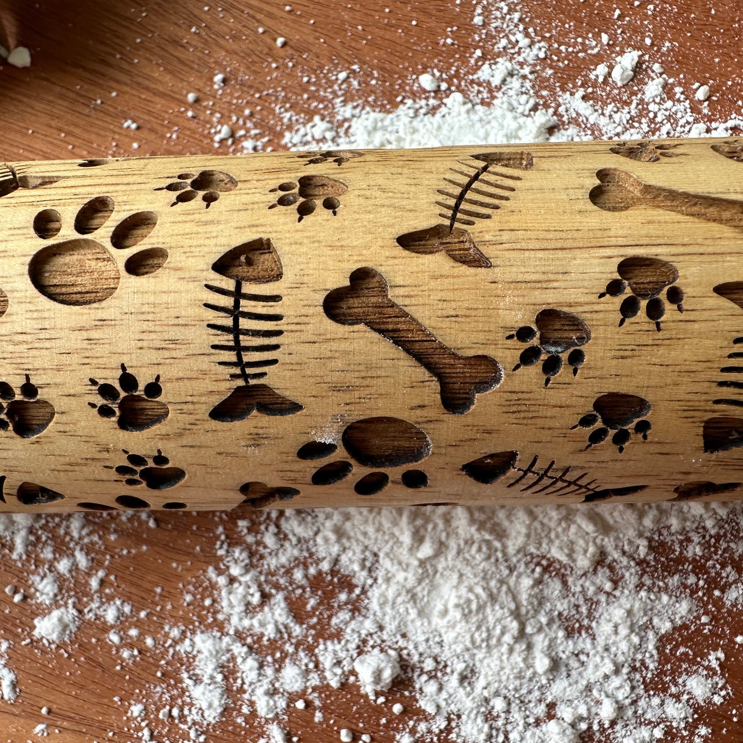 Wooden rolling pin with embossed dog-themed patterns on a flour-dusted surface.