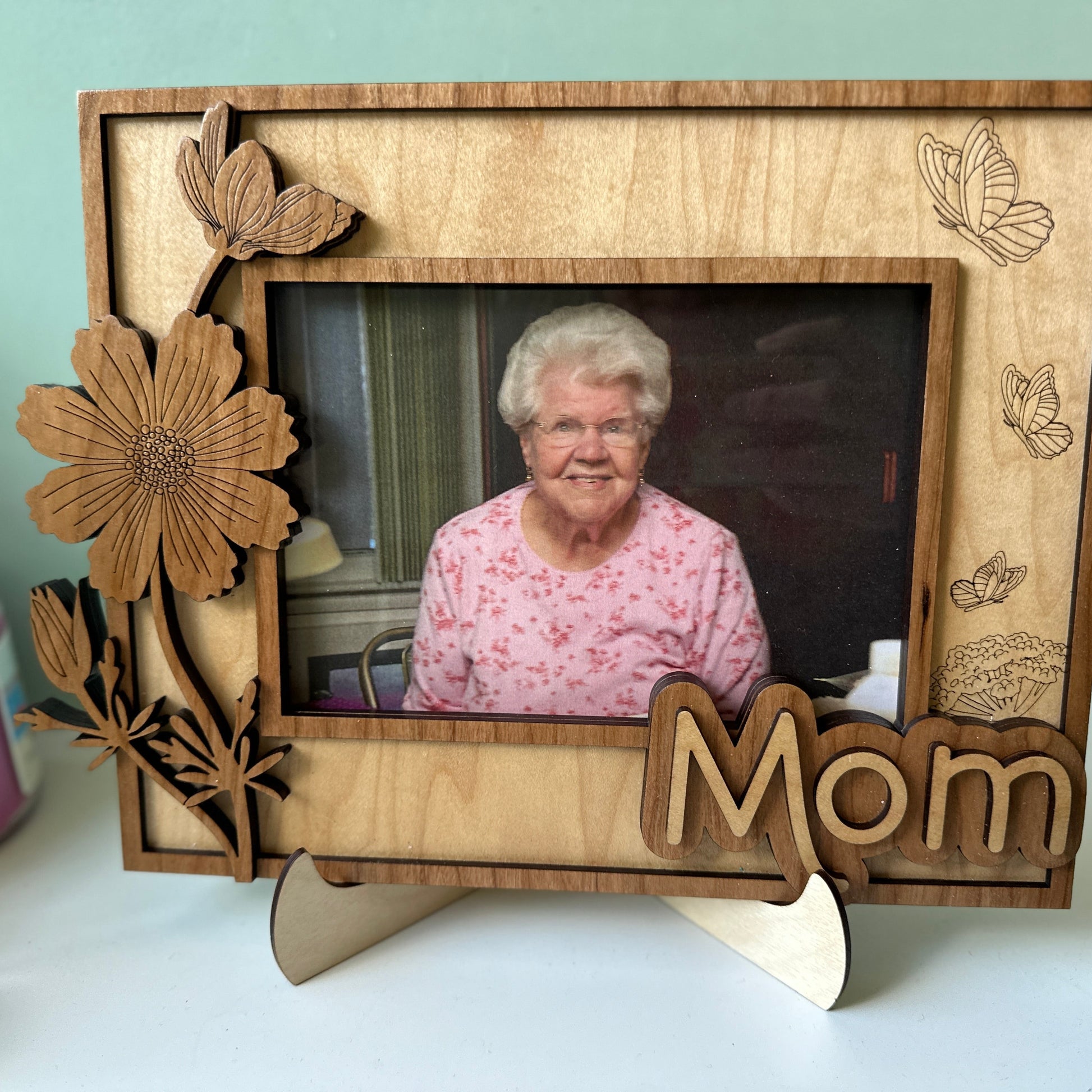 Wooden photo frame with floral designs and 'Mom' engraving, featuring a photo of an elderly woman.