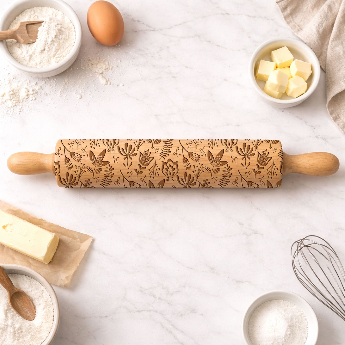Decorative rolling pin with floral patterns on a kitchen counter with baking ingredients.