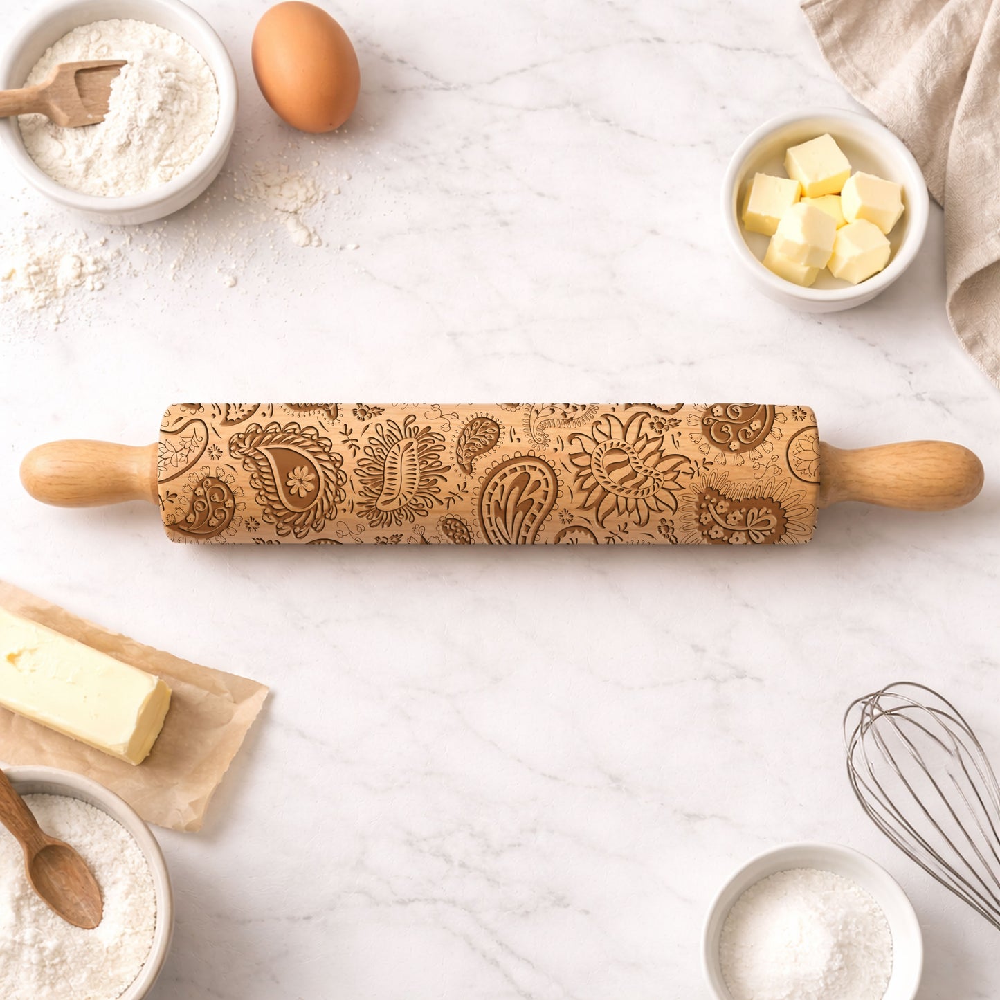 Wooden rolling pin with decorative patterns on a kitchen counter with baking ingredients.