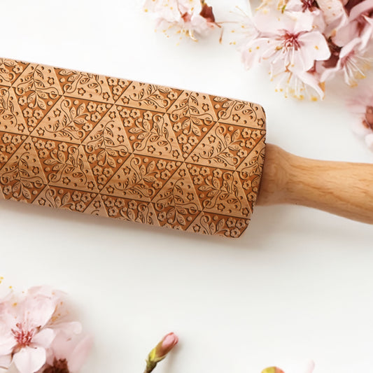 Wooden rolling pin with floral patterns on a white background with cherry blossoms.