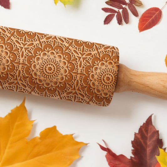 Wooden embossing rolling pin with floral patterns on a white background with autumn leaves.