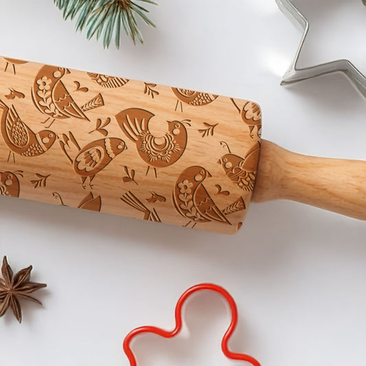 Wooden rolling pin with embossed designs on a white surface with star anise and a red cookie cutter.