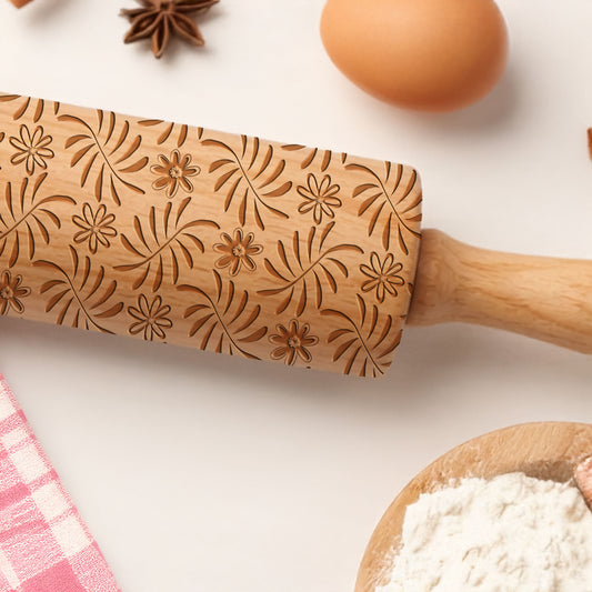 Wooden rolling pin with floral patterns on a kitchen counter with flour and eggs.