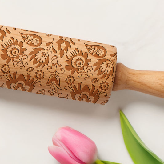 Wooden rolling pin with floral patterns next to a pink tulip on a light background
