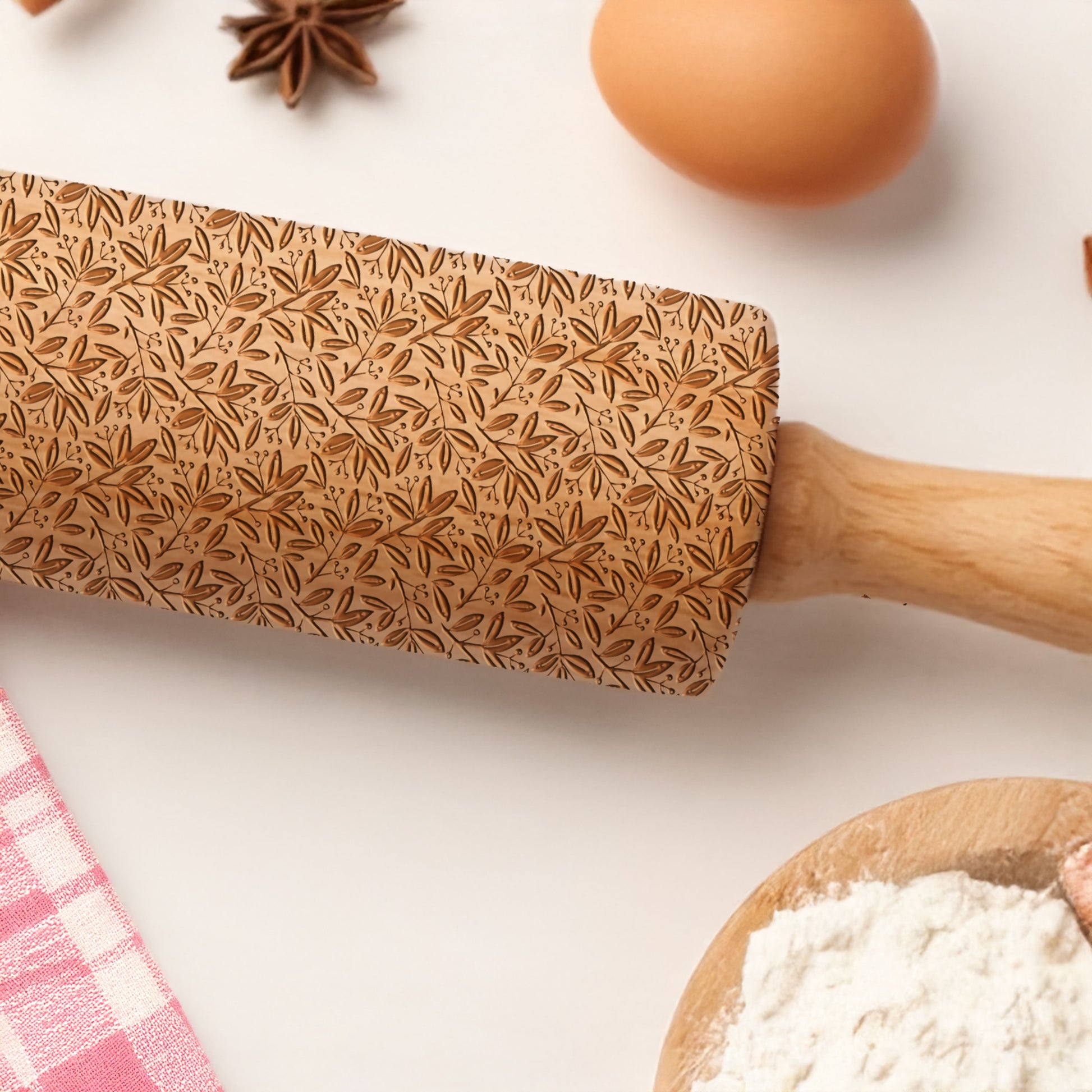 Wooden rolling pin with leaf pattern on a kitchen counter with flour and eggs.