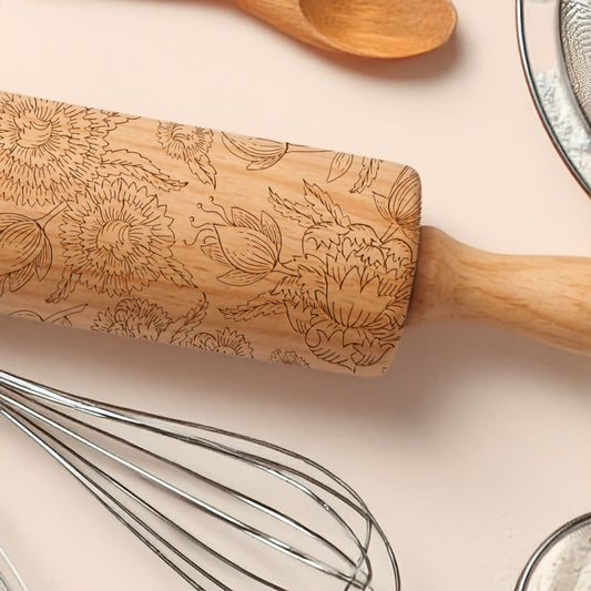Wooden rolling pin with floral patterns on a light pink surface with kitchen utensils.