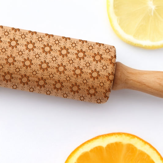 Wooden rolling pin with floral patterns on a white background with sliced oranges and lemons.