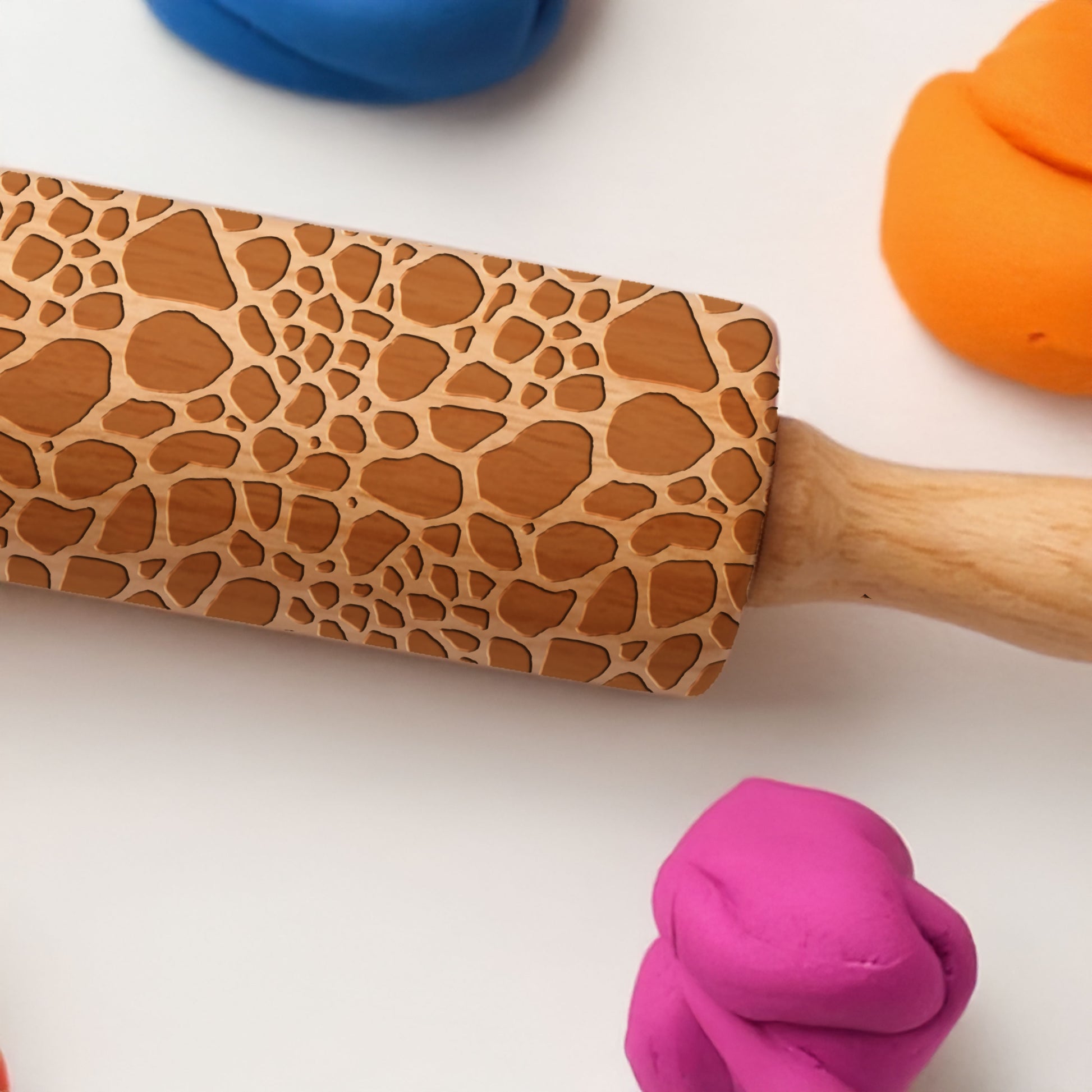 Rolling pin with giraffe pattern on a white background with colorful play dough.