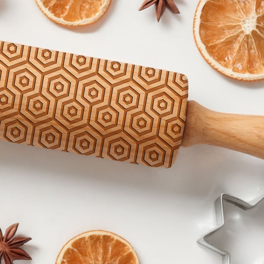 Wooden rolling pin with geometric pattern on a white surface with oranges and star anise.