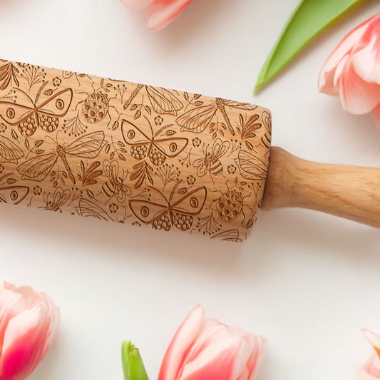 Wooden rolling pin with butterfly pattern on a white background with pink tulips