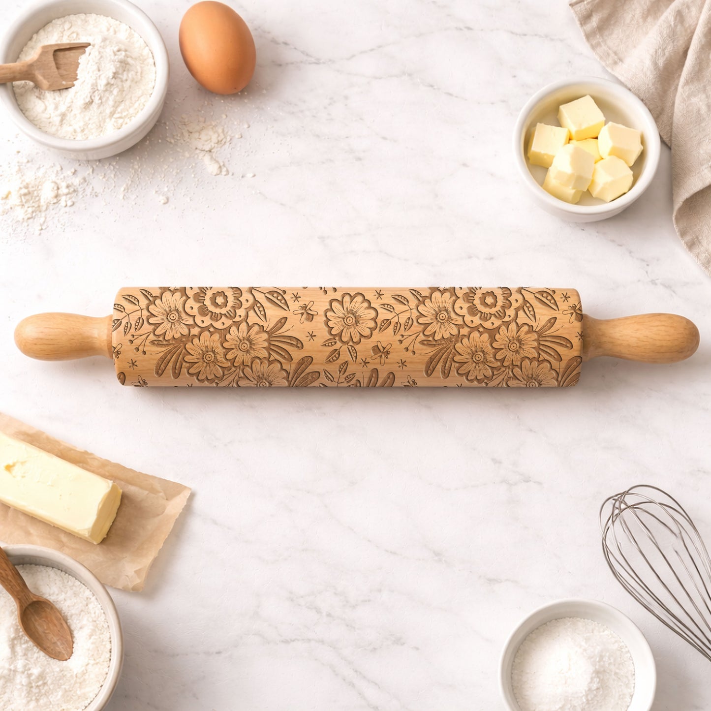 Decorative rolling pin with floral patterns on a kitchen counter with baking ingredients.