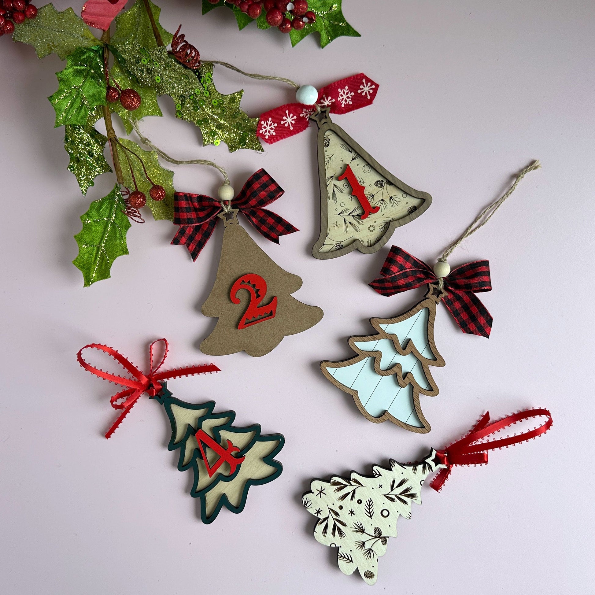 Laser-cut layered Christmas tree ornaments with red ribbon bows, hanging against a holiday backdrop