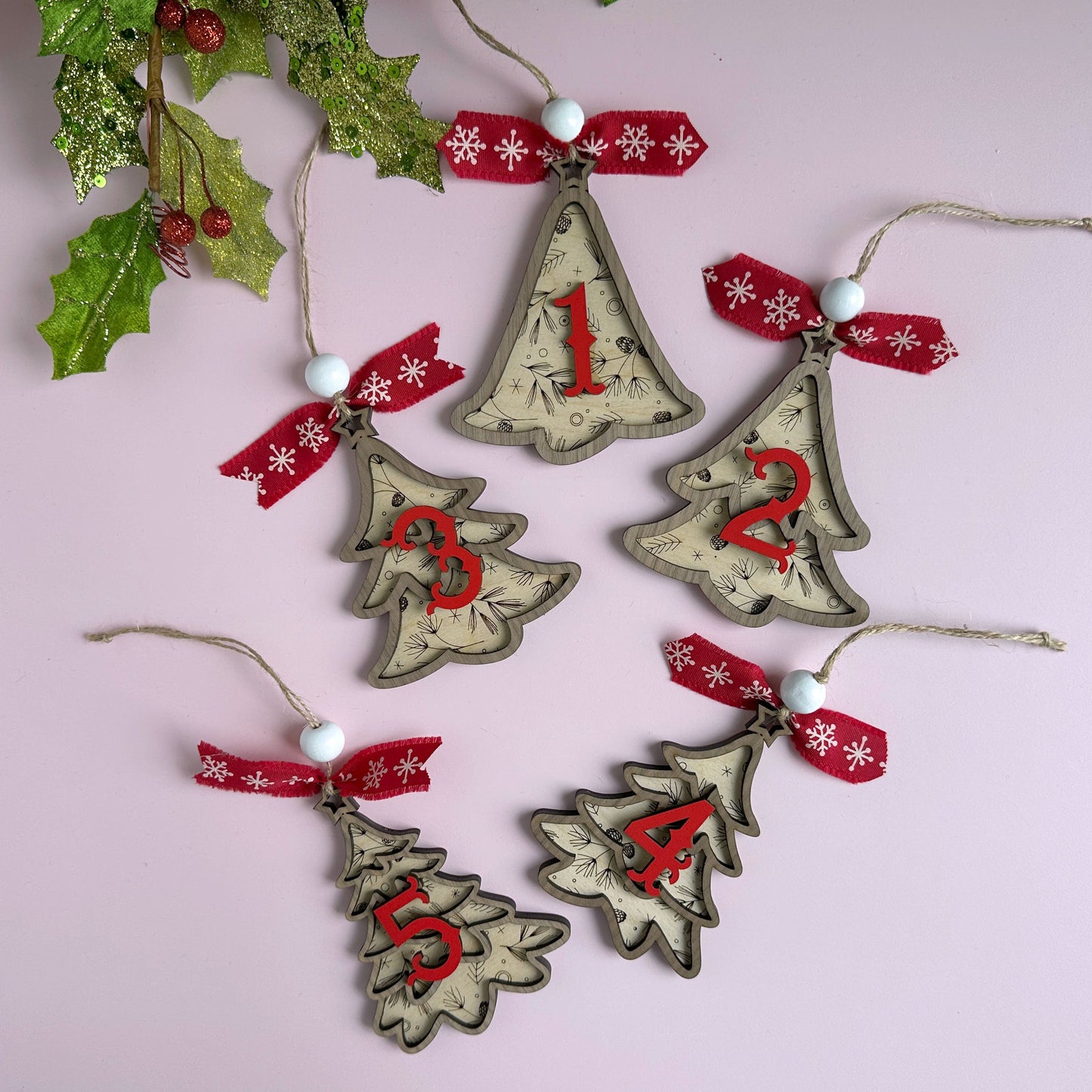 Laser-cut layered Christmas tree ornaments with red ribbon bows, hanging against a holiday backdrop