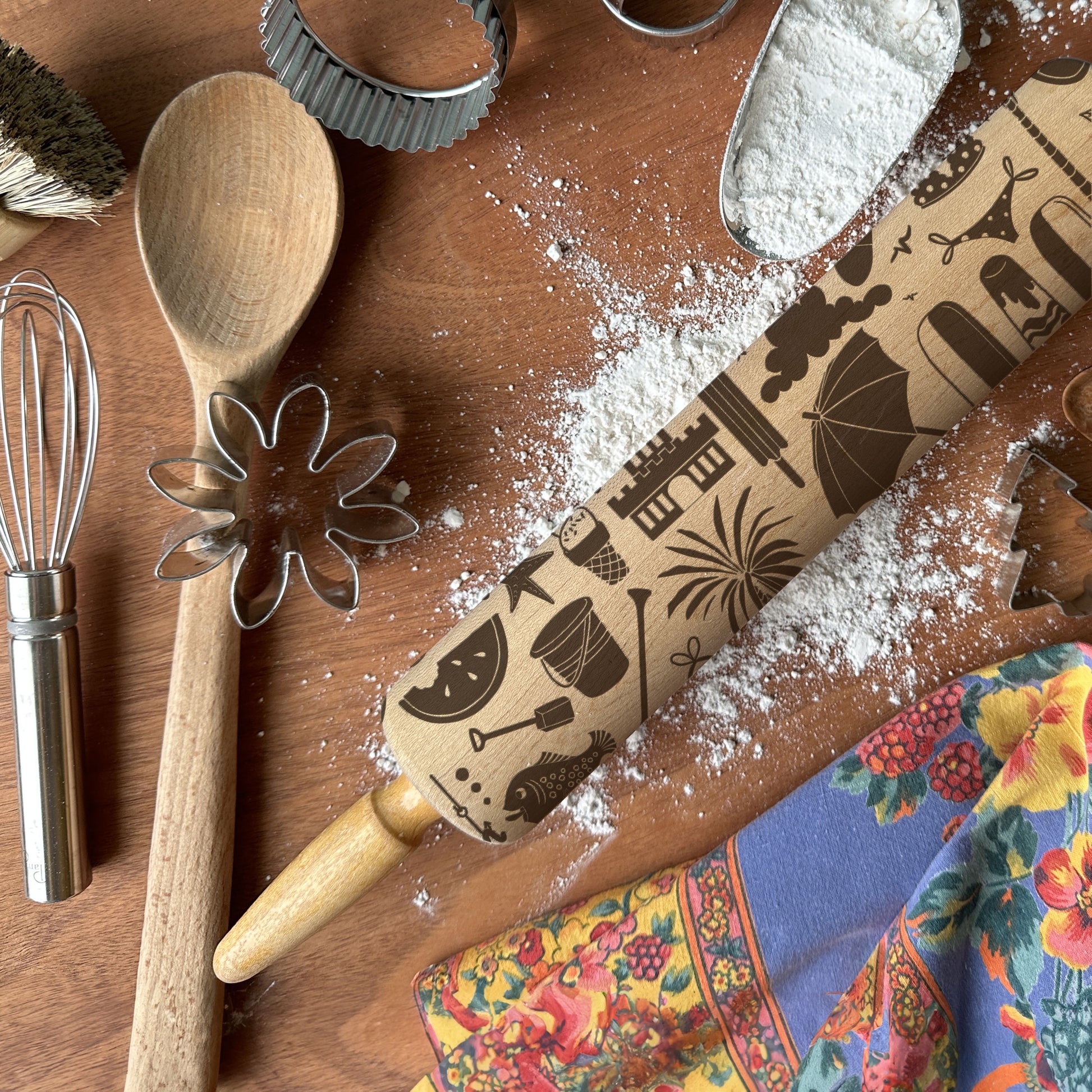Baking tools including a wooden spoon, rolling pin with decorative patterns, and cookie cutters on a flour-dusted surface.