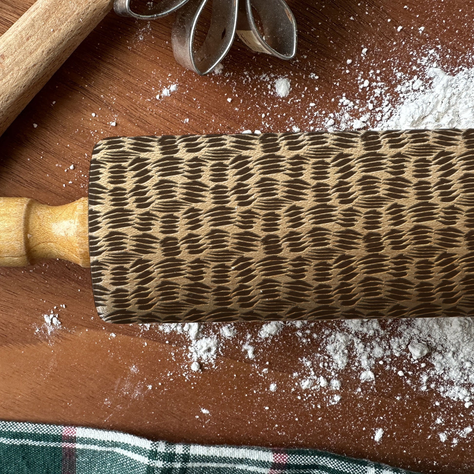 Textured rolling pin on a wooden surface with flour and kitchen tools.