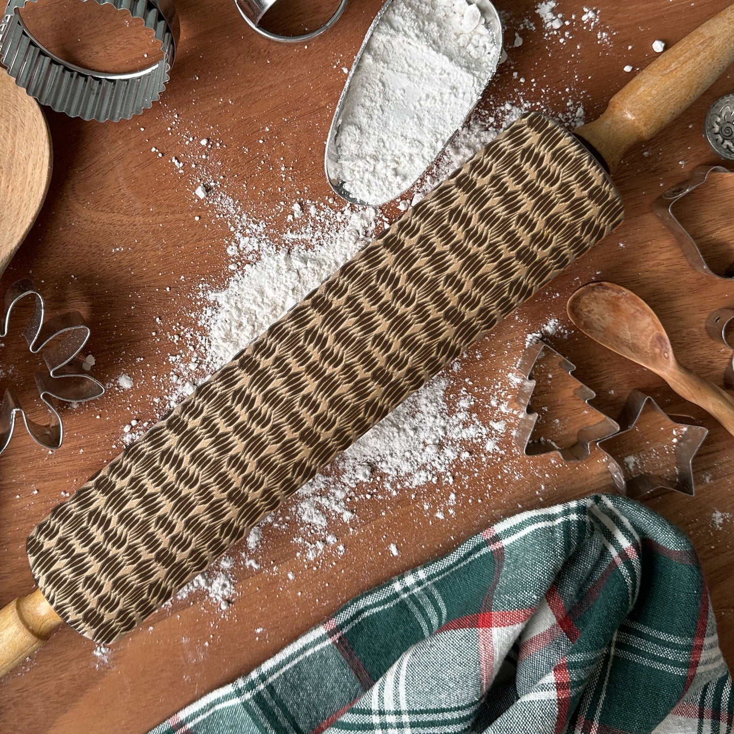 Wooden rolling pin with textured surface on a wooden surface with flour and baking tools.