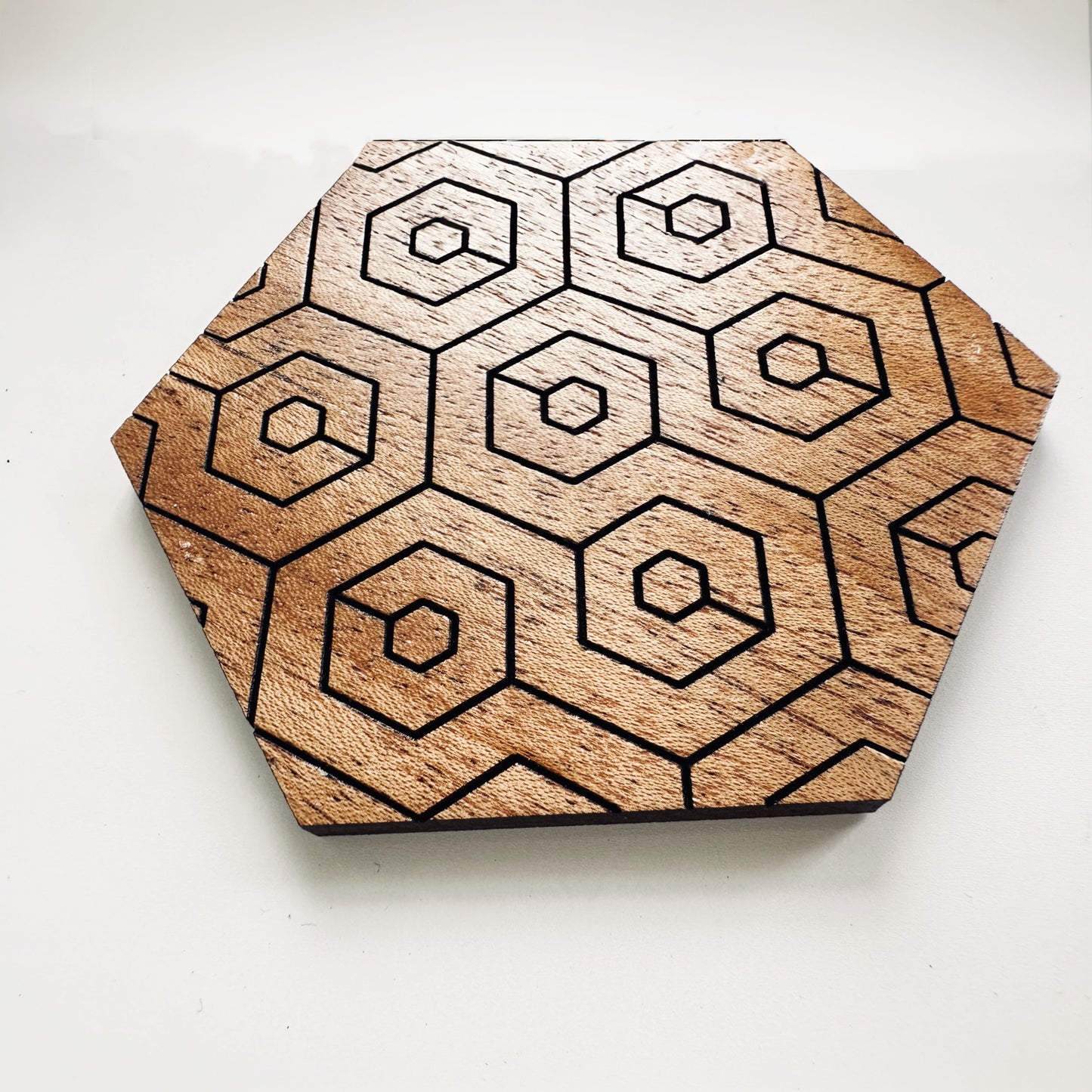 Hexagonal wooden coaster with geometric pattern on a white background